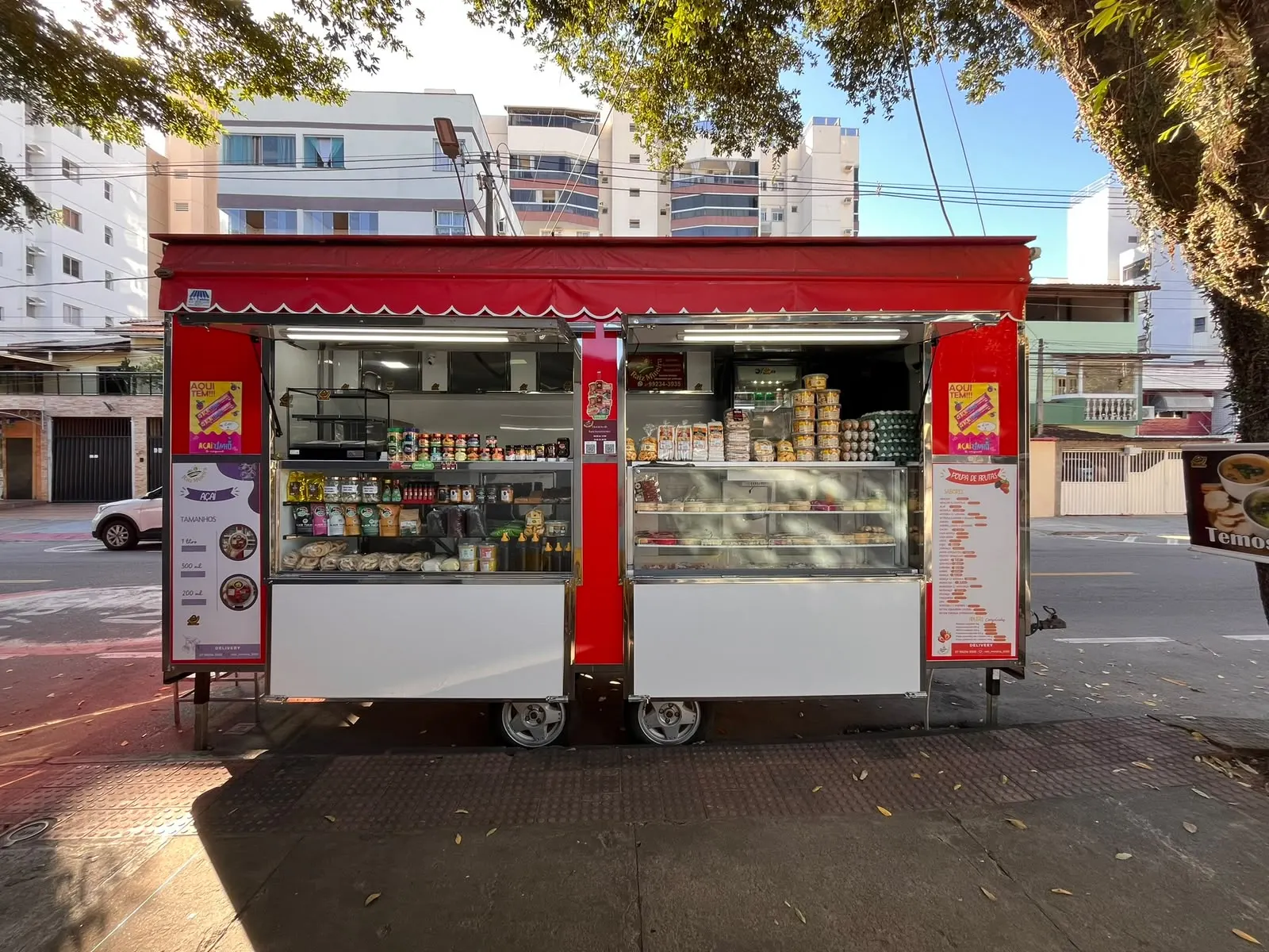 O trailer vermelho da Raiz Mineira aberto na calçada, com as prateleiras cheias.